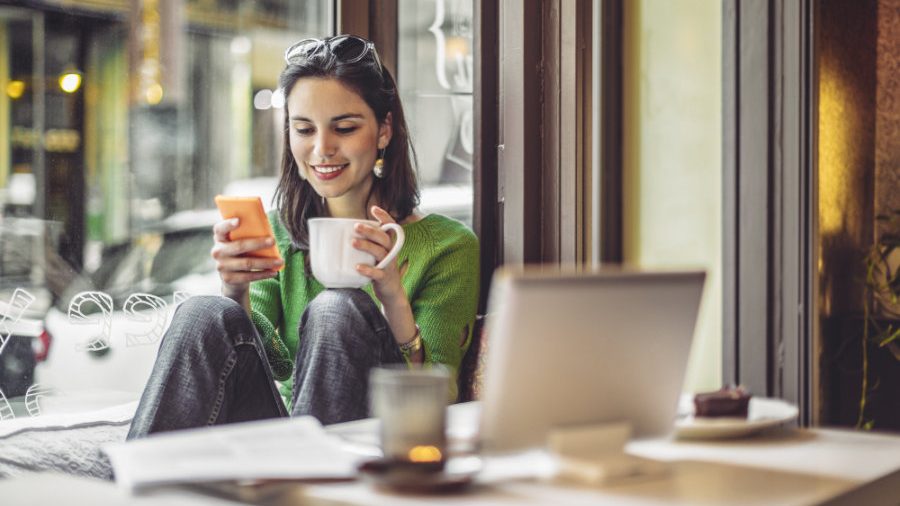 Eine Frau sitzt mit Kaffeetasse am Bürotisch und liest Arbeitgeberbewertungen zur Unternehmenskultur.